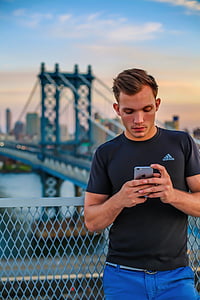 man in black Adidas shirt holding iPhone beside metal fence thumbnail