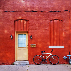 white and black bicycle parked beside red concrete house with beige wooden glass-top door and red wooden window thumbnail