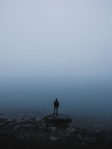 person standing on rock looking at body of water thumbnail