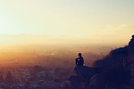 man sitting on rock on cliff overlooking plains golden hour photography thumbnail