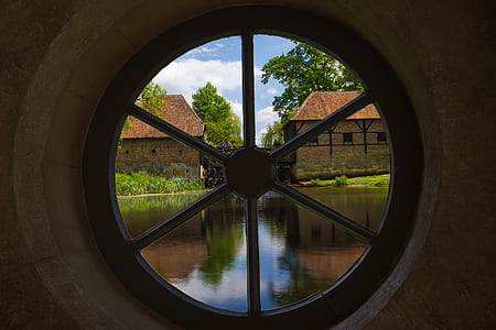 photo of lake near houses taken through round black framed clear glass window thumbnail