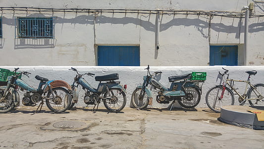 three assorted-color pedal mopeds near concrete fence during daytime thumbnail