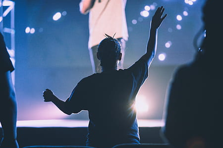 silhouette photography of person raising right hand in front of stage thumbnail