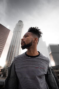 man looking right while standing concrete buildings under cloudy sky thumbnail