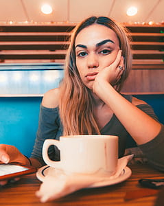 woman resting head on her left palm in front table with white ceramic cup on top thumbnail