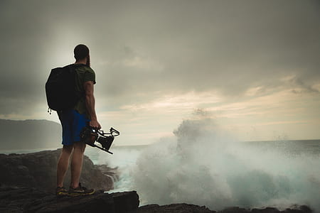 man standing on cliff while holding camera thumbnail