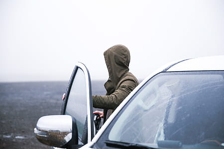 Hiker in a hooded jacket coming out of car with camera to take photographs thumbnail