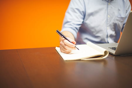 person in front of the computer writing on the paper thumbnail