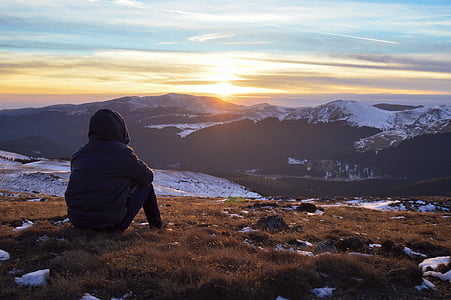person sitting on green grass overlooking snow-covered mountain during golden hour thumbnail