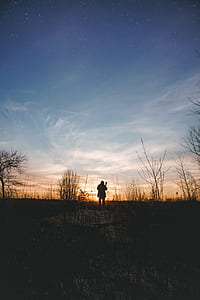silhouette photography of standing person on grass field thumbnail