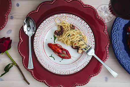 Fancy dinner with seafood pasta, crayfish and red wine by the table decorated with roses thumbnail