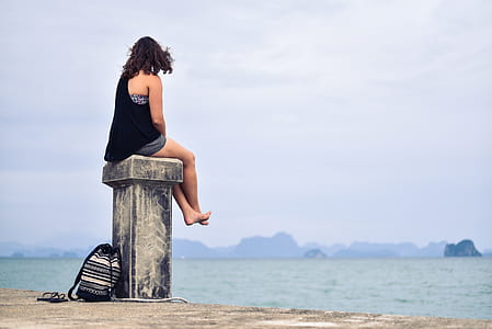 Woman in Black Shirt Sitting Near Body of Water during Daytime thumbnail