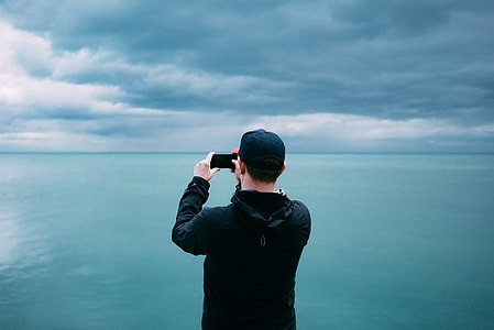 person taking photo of blue sea and white clouds during daytime thumbnail