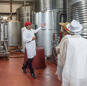 man wearing red cap and lab gown standing near large tanks thumbnail