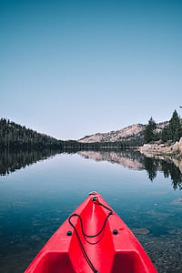 red kayak on body of water near green trees thumbnail