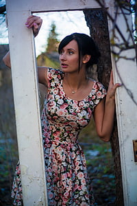woman wearing floral dress looking between white wooden door frame thumbnail