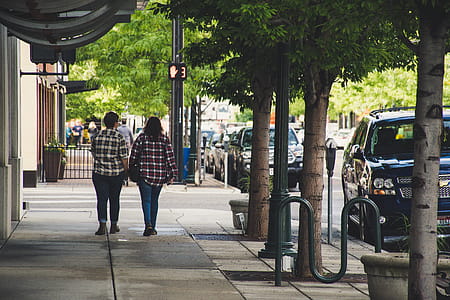 Two Woman in Plaid Sport Shirt Walking on Concrete Pathway Near Street thumbnail