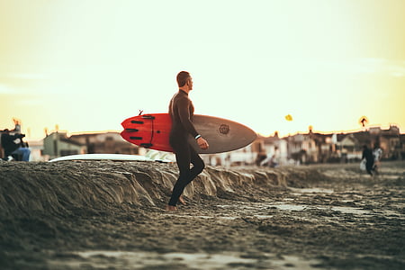 surfer in black rash guard carrying red and grey surfboard on the beach thumbnail