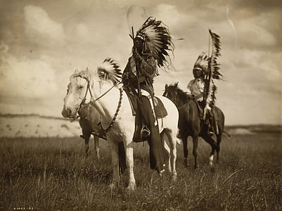 three native Americans riding on the horse on the green grass field photo thumbnail