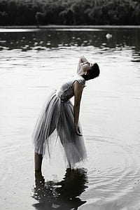 woman wearing white sleeveless dress standing on body of water bending her body thumbnail