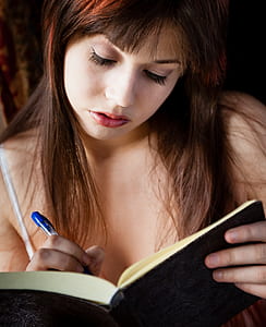 woman holding blue ballpoint pen and black book thumbnail