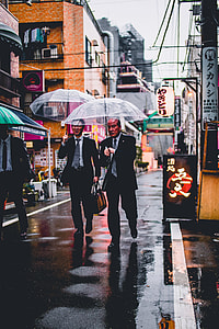 three man wearing black suits holding umbrella walking on street thumbnail
