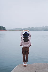 woman standing on concrete edge near lake thumbnail