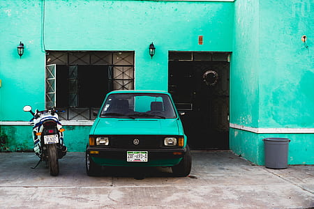 green Volkswagen Golf parked beside white sports bike near green concrete building thumbnail