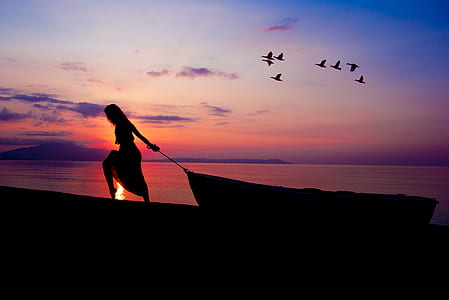 silhouette of woman pulling boat on shore during sunset thumbnail