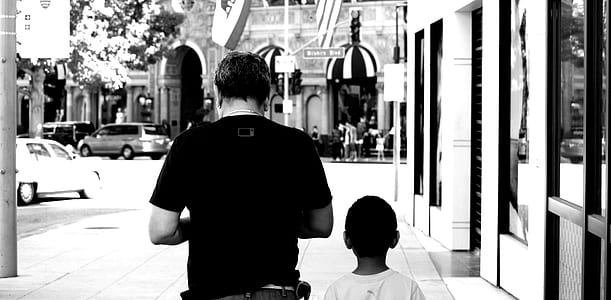 grayscale photo of man and boy walking beside building thumbnail