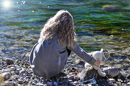 woman sitting beside animal plush toy near body of water thumbnail
