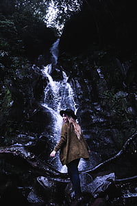woman in brown jacket and black hat near waterfalls thumbnail