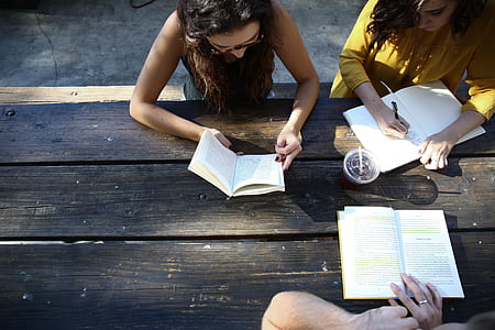 woman reading book beside woman writing at daytime thumbnail