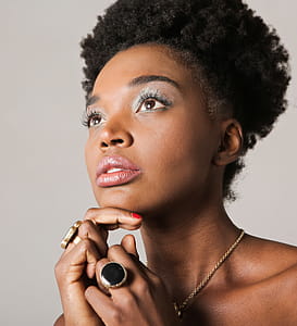 A young African woman wearing jewelry posing indoors with her fingers on her chin thumbnail