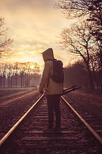 man standing on rail while holding tripod stand during golden hour thumbnail