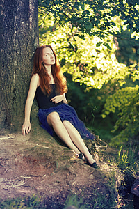 woman in black sleeveless top and blue skirt sitting under the tree thumbnail