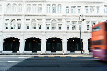 orange bus passing through white building thumbnail