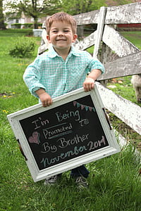 smiling boy holding photo frame outdoor near white wooden fence during daytime thumbnail