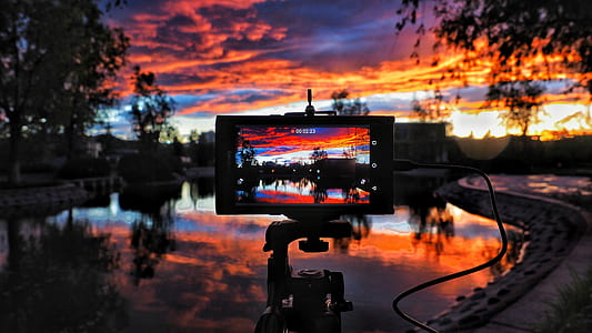 camera on tripod taking picture of lake during sunset thumbnail