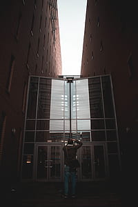 man standing on grass door between buildings during daytime thumbnail