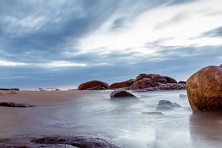 rocks on beach under cloudy blue sky thumbnail