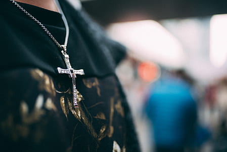 person wearing silver-colored cross pendant necklace thumbnail