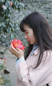 woman smelling and holding pink camellia flower thumbnail