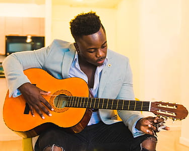 Man Wearing Blue Coat and Black Distressed Bottoms Holding Brown Classical Guitar thumbnail