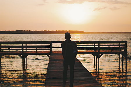 man standing on dock facing body of water thumbnail