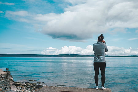 woman taking photo of the ocean under blue sky thumbnail