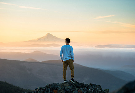 man in blue long-sleeved shirt standing on mountain during daytime thumbnail