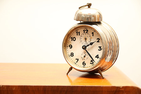 round gold-colored framed analog alarm clock on brown wooden surface thumbnail