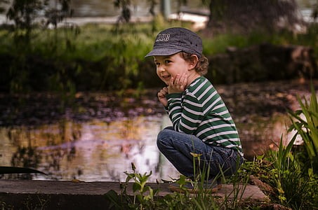selective focus photo of a boy squatting near body of water thumbnail