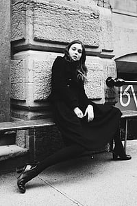woman in black dress sitting on bench beside wall thumbnail